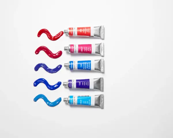Des tubes de gouache Caran d'Ache rouge, magenta, bleu outremer, violet et cyan, avec des coulées de peinture sur fond blanc. Quelle peinture pour toile ?