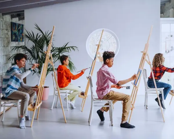 Des enfants concentrés sur leur peinture sur petite toile facile, chacun sur son chevalet, dans un atelier lumineux.