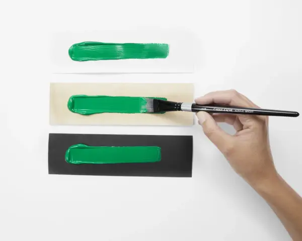Bandes de peinture acrylique verte sur papier blanc, bois et noir. Une main tient un pinceau, montrant l'application de l'acrylique avant ou après peinture.