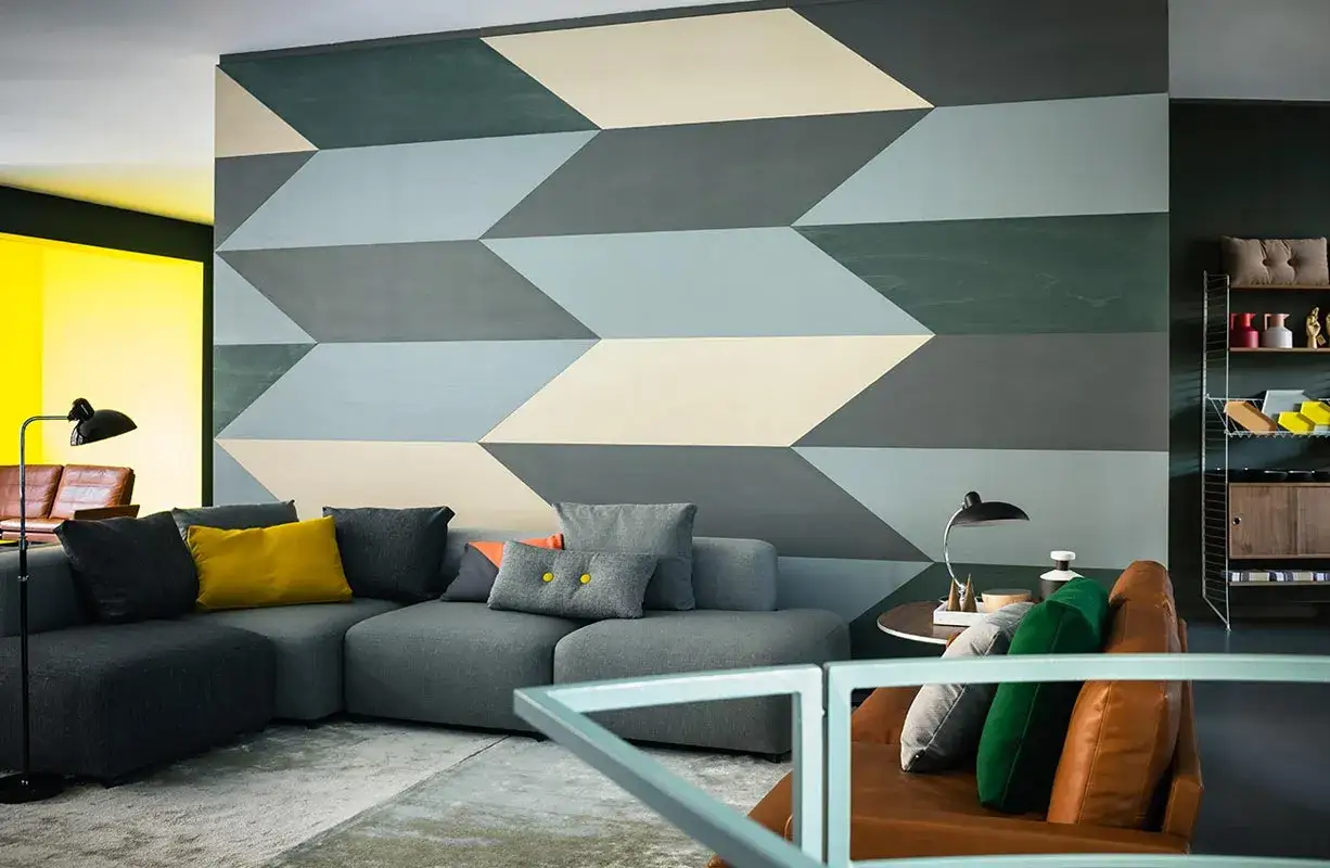 Un salon moderne avec un canapé gris, des coussins colorés et un mur orné d'un audacieux modèle de peinture géométrique en dégradé de bleus et gris.